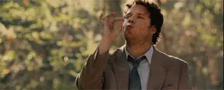 A man in a suit pulling on a joint and dancing comfortably, surrounded by nature.